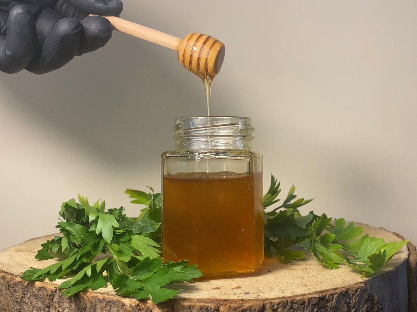 honey dripping in a jar with a honey dipper surrounded by a wood log and some rapesseed flowers.